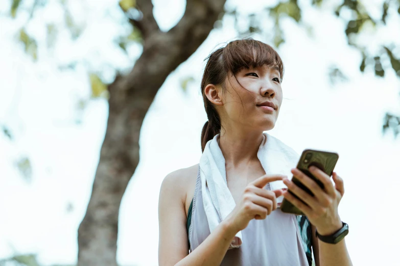 a woman with a towel around her neck looking at a cell phone, trending on pexels, sydney park, wearing fitness gear, ethnicity : japanese, background image