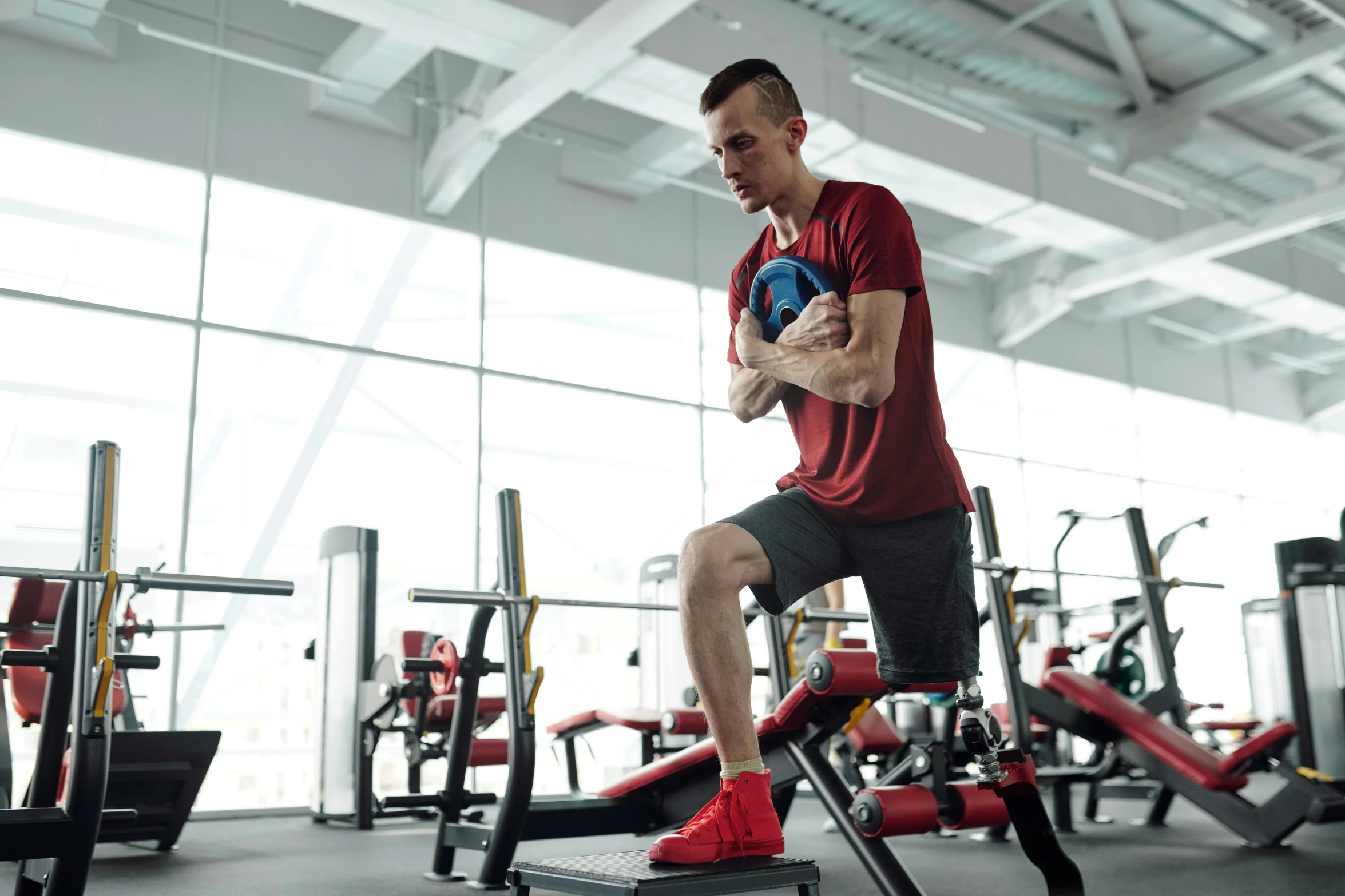 a man is squatting on a bench in a gym, pexels contest winner, red sport clothing, square, no watermarks, in style of kyrill kotashev
