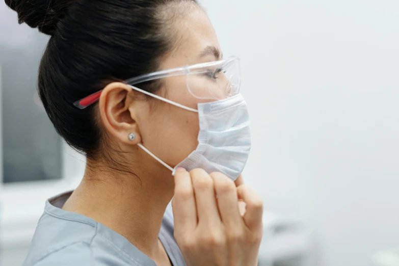 a woman wearing a face mask while brushing her teeth, trending on pexels, wearing lab coat and glasses, close up shot from the side, asian face, surgical gown and scrubs on