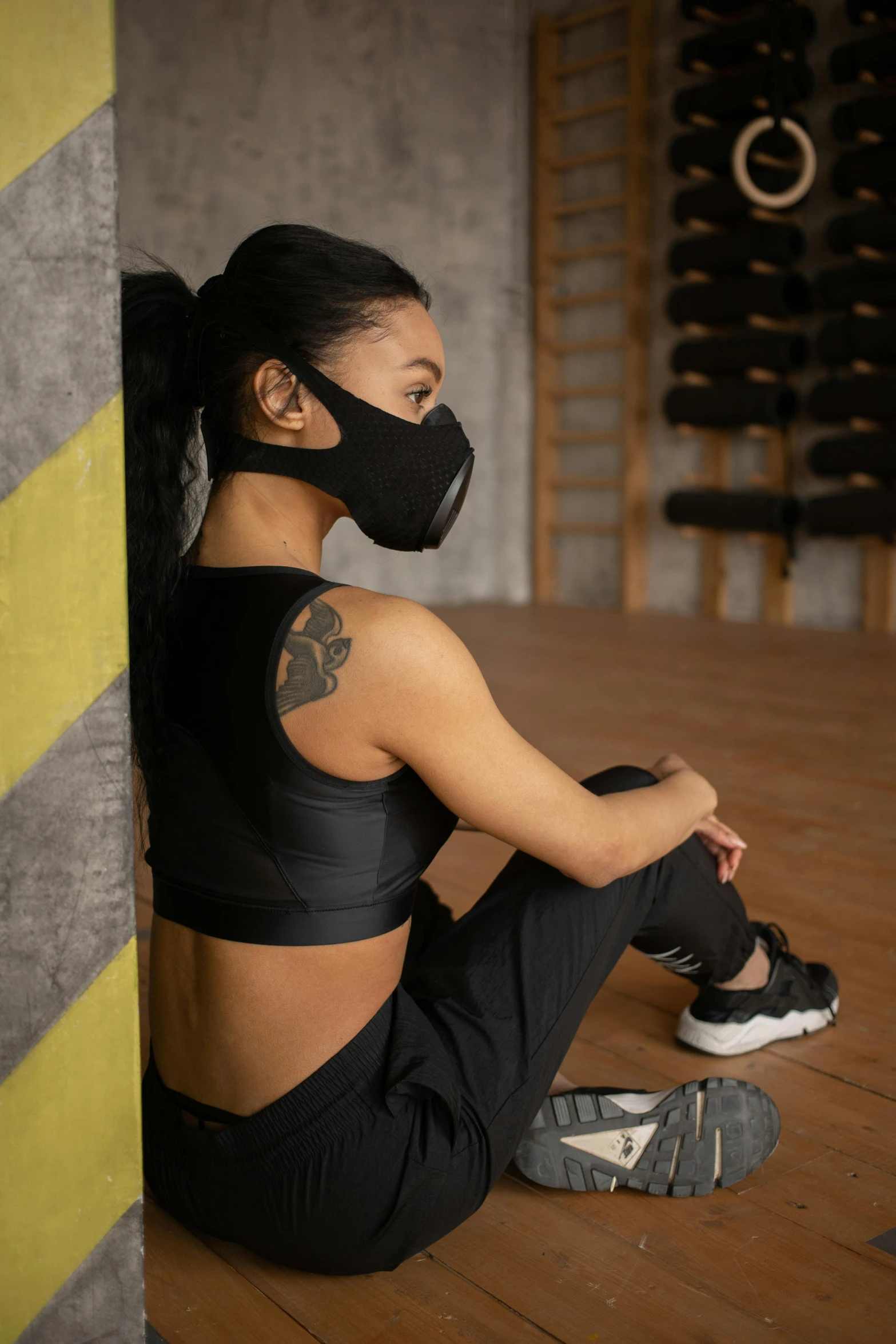 a woman sitting on the floor wearing a mask, detailed sports bra, wearing all black mempo mask, profile image, synthetic skin