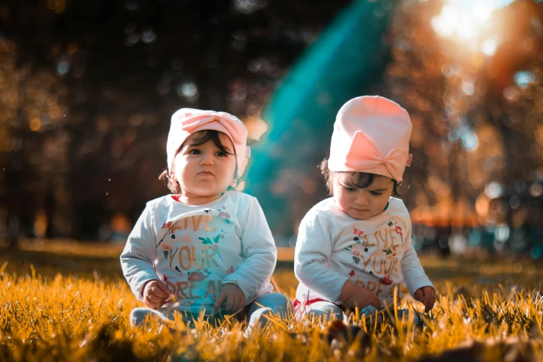 a couple of babies sitting on top of a lush green field, pexels contest winner, symbolism, avatar image, cute hats, strong sunlight, on ground
