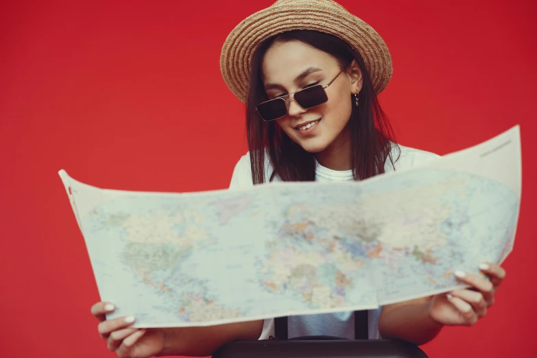 a woman in a hat and sunglasses looking at a map, pexels contest winner, in red background, casually dressed, 🦩🪐🐞👩🏻🦳, pilot girl