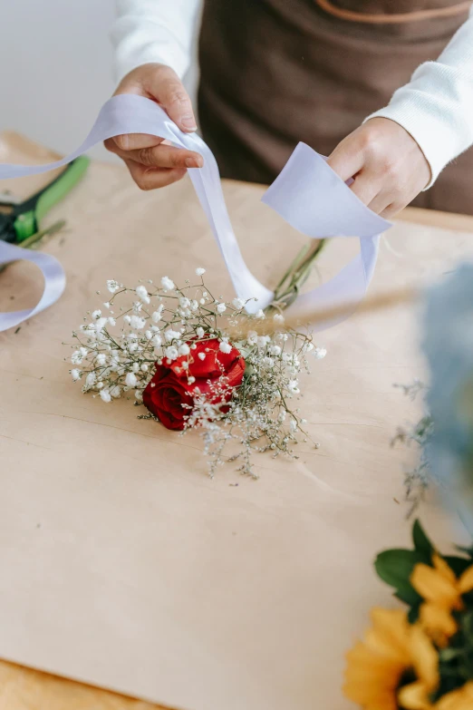 a woman holding a piece of paper near a bunch of flowers, a still life, by Matthias Stom, trending on unsplash, romanticism, ribbon, detail shot, groom, blue and white and red mist