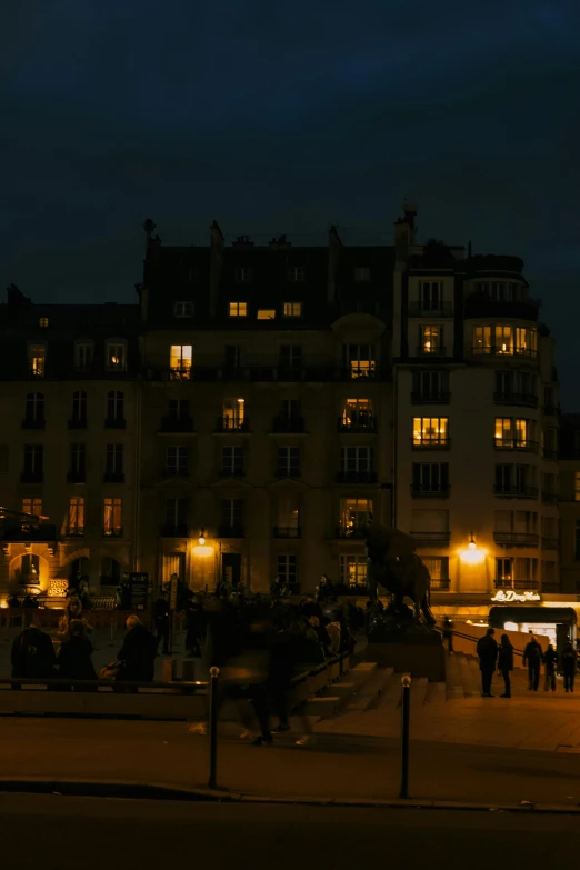 a group of people walking down a street at night, paris school, beautifully lit buildings, panorama, square, 8k 50mm iso 10