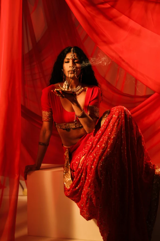 a woman in a red sari sitting on a stool, smoking weed, cinematic and dramatic red light, wearing an ornate outfit, ( ( theatrical ) )