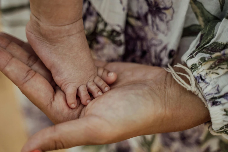 a close up of a person holding a baby's hand, trending on pexels, barefoot, with intricate details, warm coloured, handcrafted