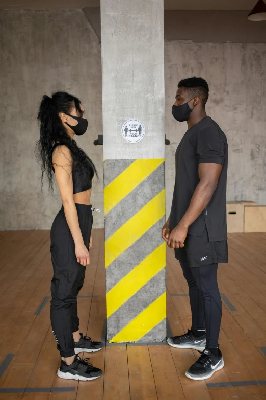 a man and a woman standing next to each other, trending on pexels, masked person in corner, black human spine, two piece workout clothes, industrial aesthetic