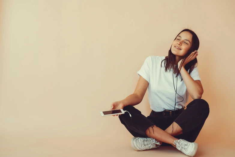 a woman sitting on the floor listening to music, trending on pexels, aestheticism, maisie williams, plain background, earbuds, no - text no - logo