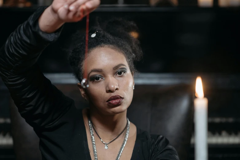 a woman holding a string with a candle in the background, a portrait, trending on pexels, renaissance, black jewellery, thumbnail, mixed race woman, female occultist