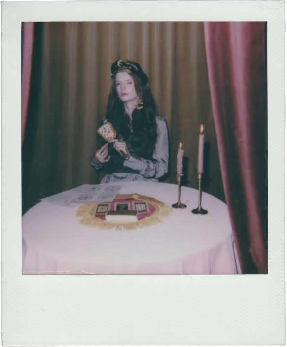 a woman sitting at a table in front of a cake, a polaroid photo, unsplash, magic realism, dressed as an oracle, with victorian clothing, lorde, high quality photo