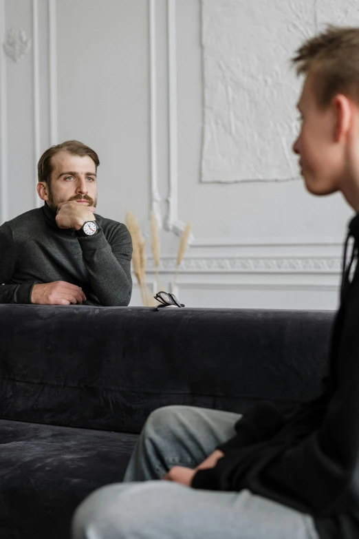 two men sitting on a couch in a living room, by Adam Marczyński, trending on pexels, in a meeting room, thin young male, pondering, on a gray background