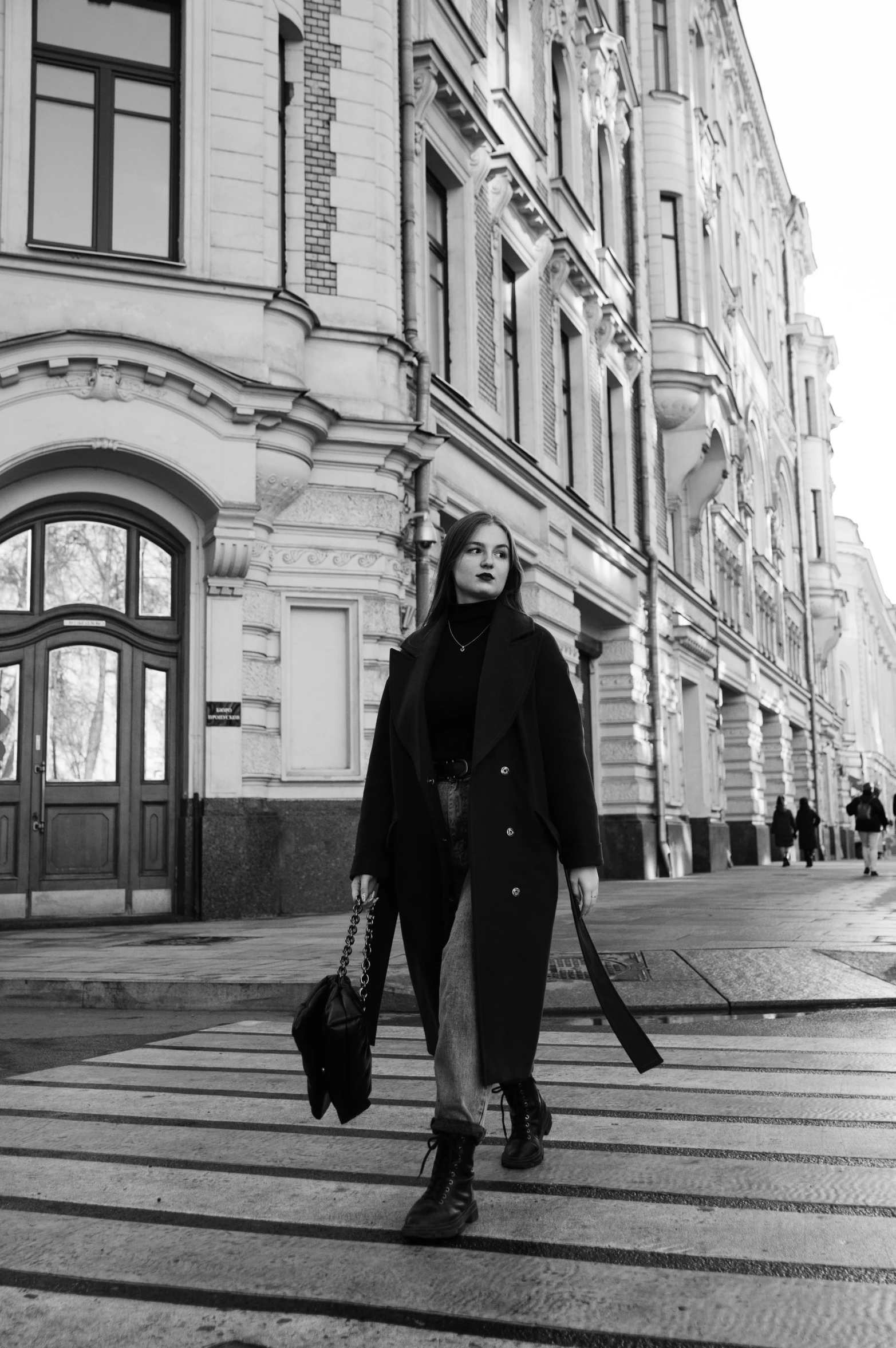 a black and white photo of a woman walking down a street, inspired by Andrei Ryabushkin, 🤤 girl portrait, ( ( wearing a long coat ) ), on a great neoclassical square, nikolay