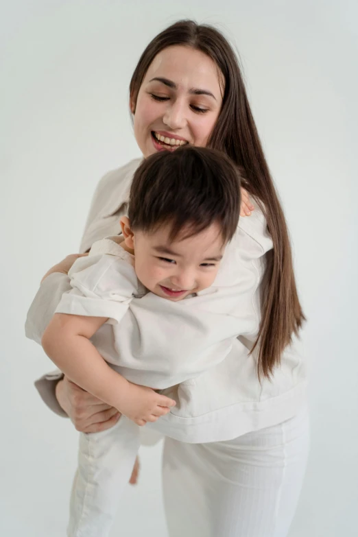 a woman holding a child in her arms, inspired by Oswaldo Viteri, pexels contest winner, mingei, wearing a light shirt, plain background, softplay, ruan jia and brom