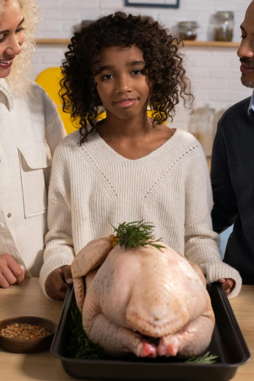 a group of people standing around a turkey, front facing the camera, at the counter, little kid, promo image