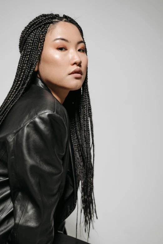 a woman in a black leather jacket sitting on a stool, inspired by Kim Tschang Yeul, trending on pexels, long cornrows, a portrait of issey miyake, ethnicity : japanese, profile image