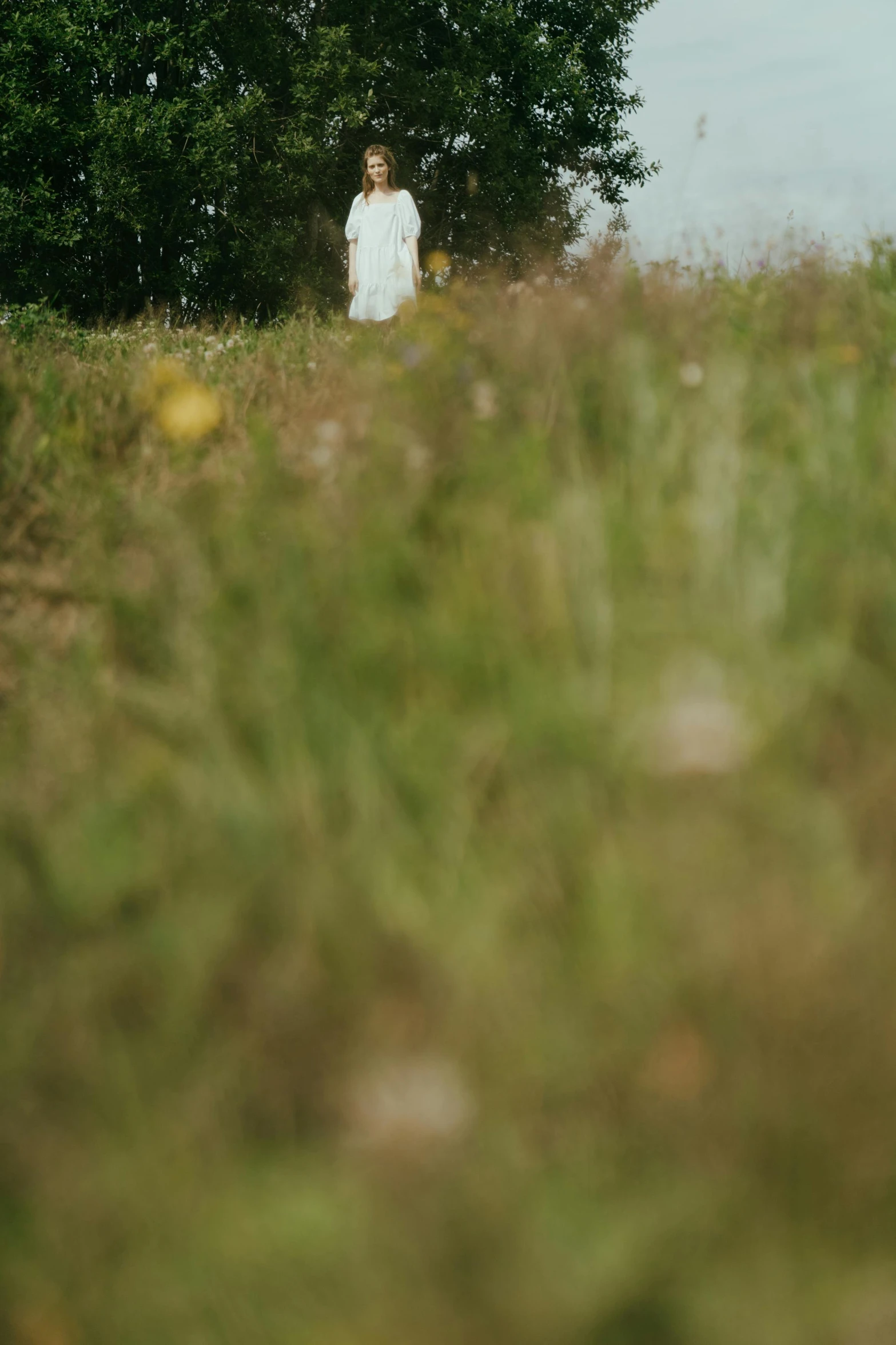 a woman in a white dress standing in a field, by Peter Churcher, unsplash, blurry footage, long thick grass, church in the background, shot with hasselblad