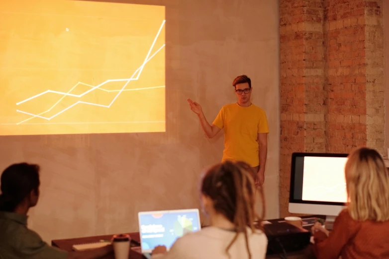 a man giving a presentation to a group of people, by Attila Meszlenyi, unsplash, yellow, programming, ignant, studio orange