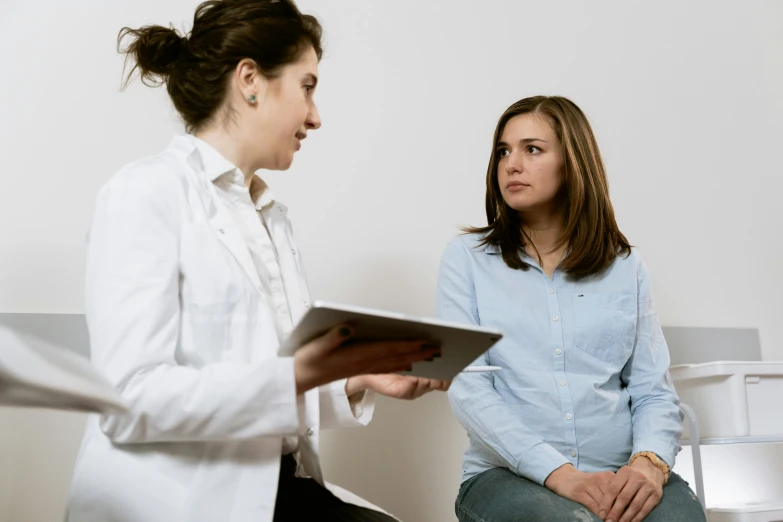 a woman sitting in a chair talking to another woman, a picture, pexels, hurufiyya, doctor, background image, in white room, gif