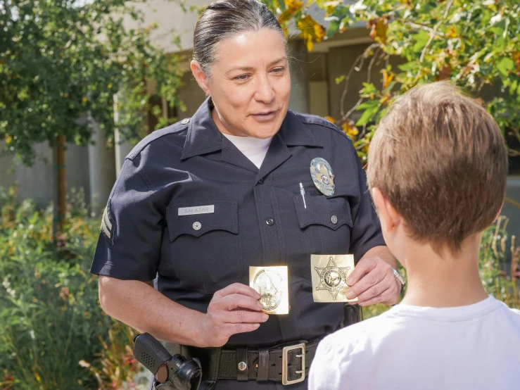 a police officer talking to a young boy, by Jennifer Bartlett, shutterstock, symbolism, high school badge, still image from tv series, actress, panoramic shot