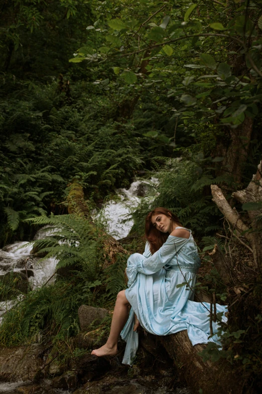 a woman sitting on a rock next to a river, inspired by Elsa Bleda, renaissance, jungle gown, slide show, blue, low quality photo