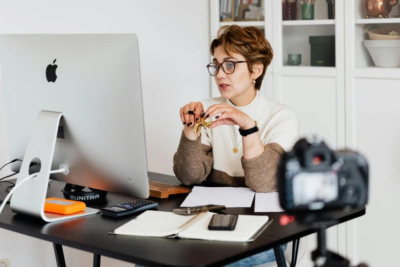 a woman sitting at a desk in front of a computer, by Julia Pishtar, trending on pexels, wearing square glasses, nicovideo, lawther sit at table playing dnd, camera looking up at her