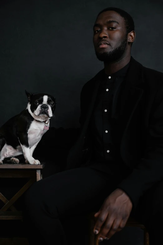 a man sitting on a chair next to a dog, an album cover, inspired by Theo Constanté, trending on unsplash, black haute couture, panel of black, french bulldog, black skin