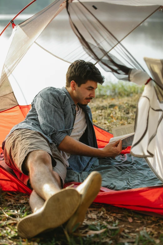 a man sitting in a tent reading a book, a portrait, trending on unsplash, sleeping bag, slide show, laying down, flirting