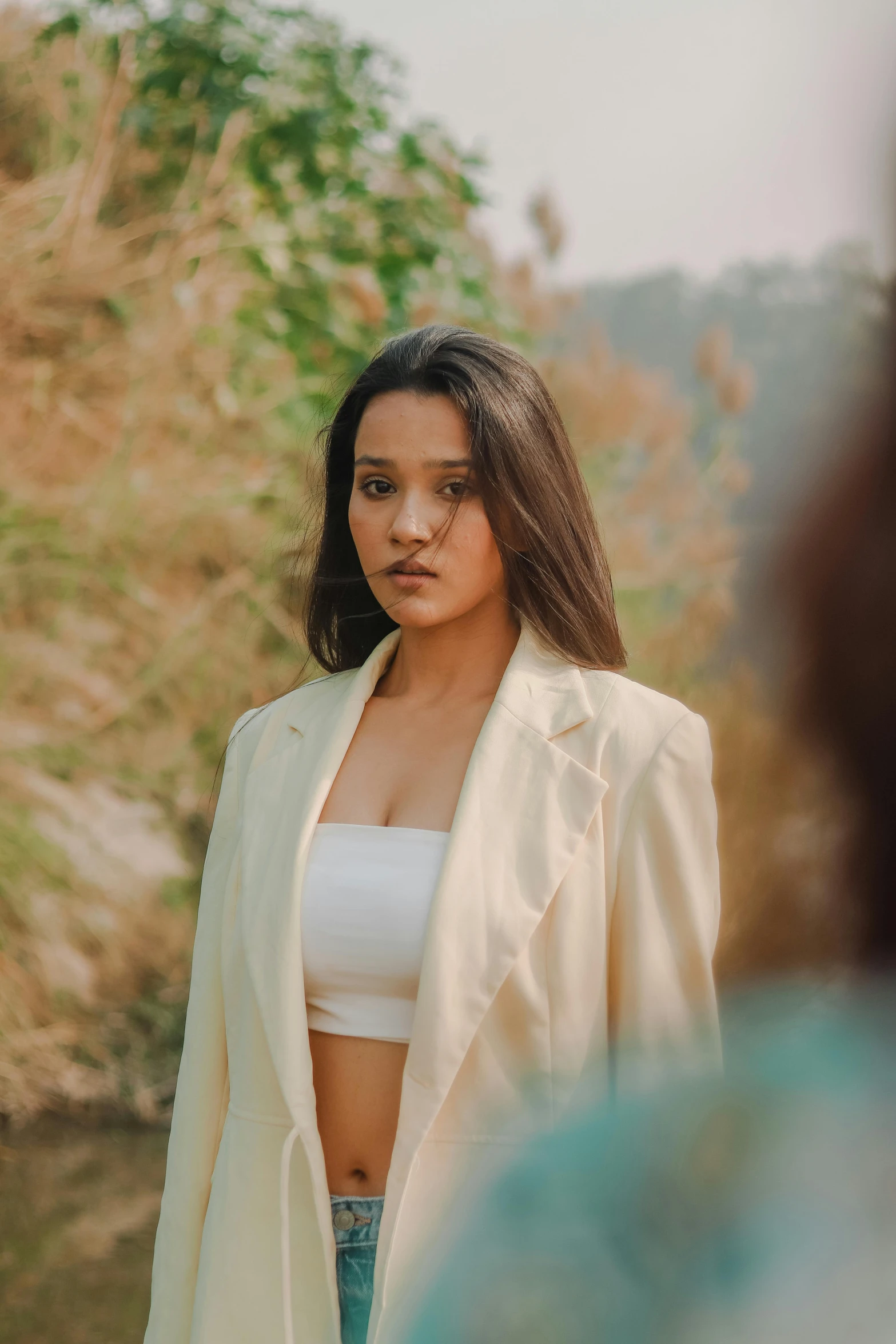 a woman standing in front of a body of water, an album cover, unsplash, beautiful young himalayan woman, wearing white suit, open jacket, angry look