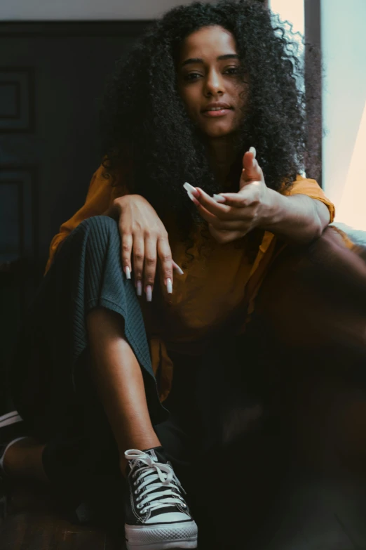 a woman sitting on a couch in front of a window, by Lily Delissa Joseph, trending on pexels, black hands with black claws, sitting dynamic pose, curls, with index finger