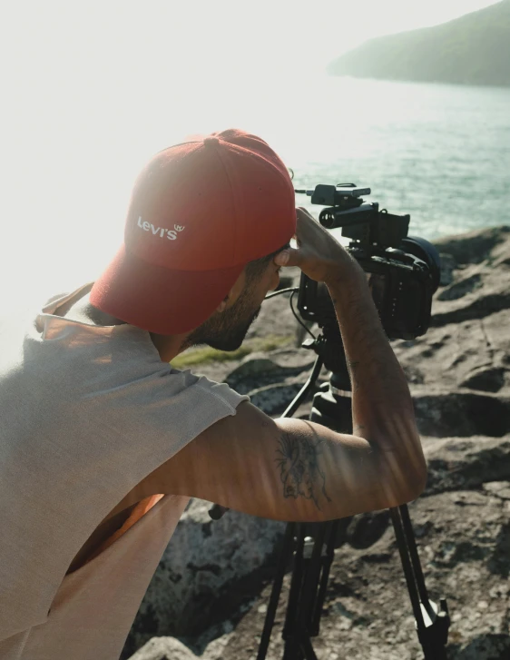 a man taking a picture of a body of water, pexels contest winner, video art, wearing a red backwards cap, tv production, modeling shoot, lgbtq