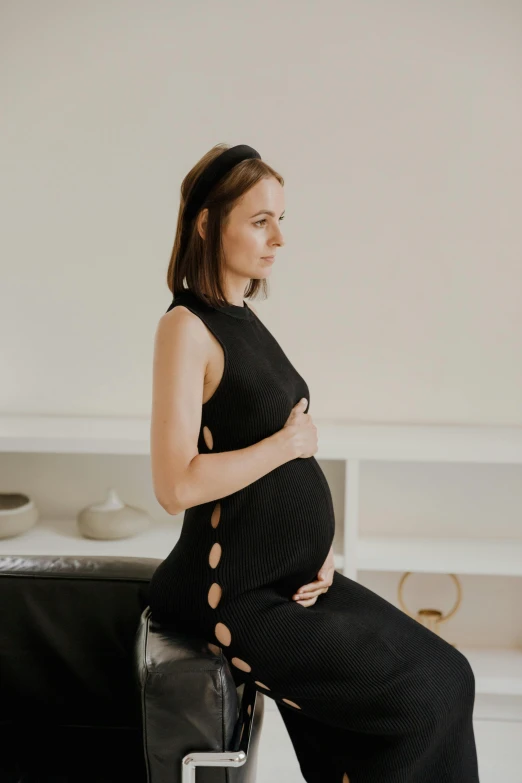 a pregnant woman in a black dress sitting on a chair, trending on pexels, renaissance, from side, neoprene, organic dress, maternal