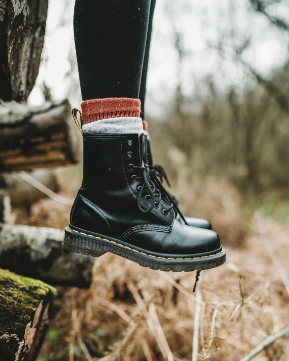 a person standing on a log in the woods, inspired by Elsa Bleda, unsplash contest winner, doc marten boots, wearing in stocking, profile image, black and terracotta