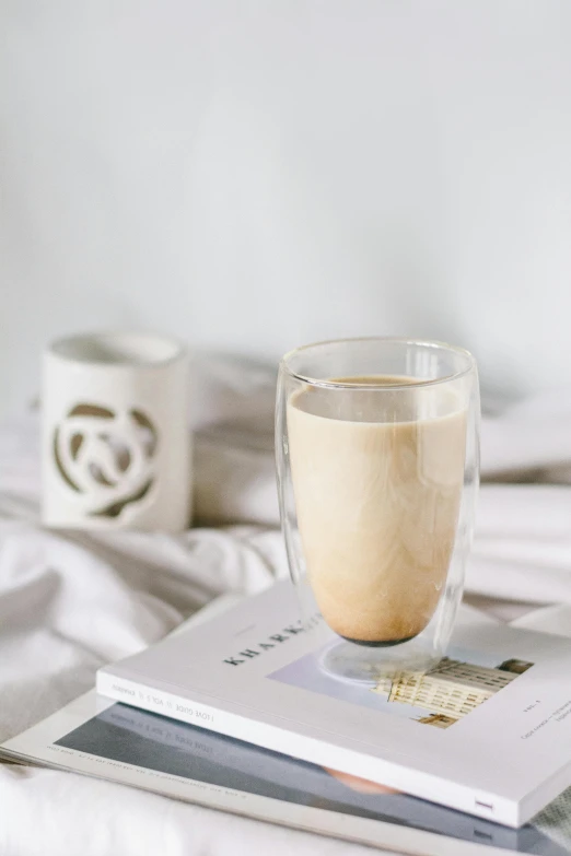 a book sitting on top of a bed next to a cup of coffee, iced latte, textured base ; product photos, amber glasses, beige