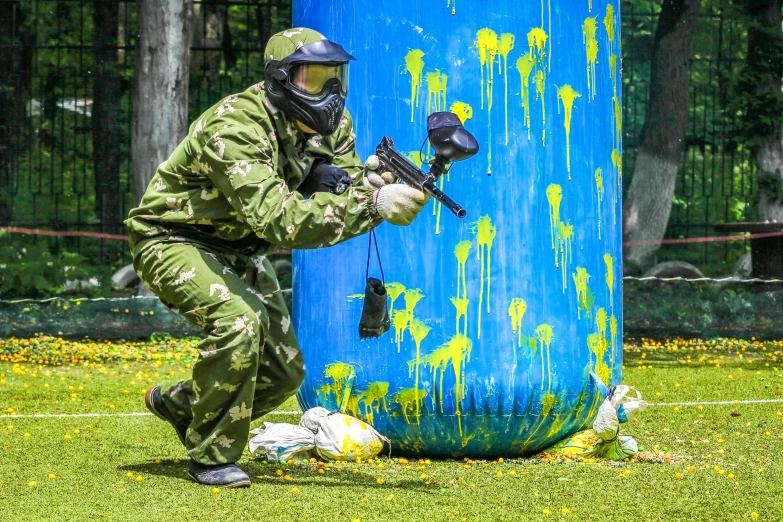 a man in camouflage is playing paintball, by Julia Pishtar, pixabay, action painting, some yellow green and blue, jc park, in front of a round, body covers with neon flowers
