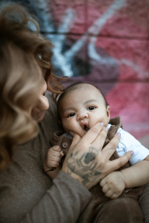 a woman holding a baby in her arms, by Elsa Bleda, pexels contest winner, hand on his cheek, tattooed, brown, 8 1 5