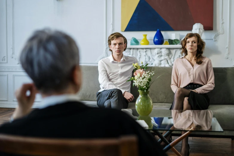 a man and a woman sitting on a couch in a living room, by Jaakko Mattila, pexels contest winner, hyperrealism, in a meeting room, 3 actors on stage, parents watching, on a white table