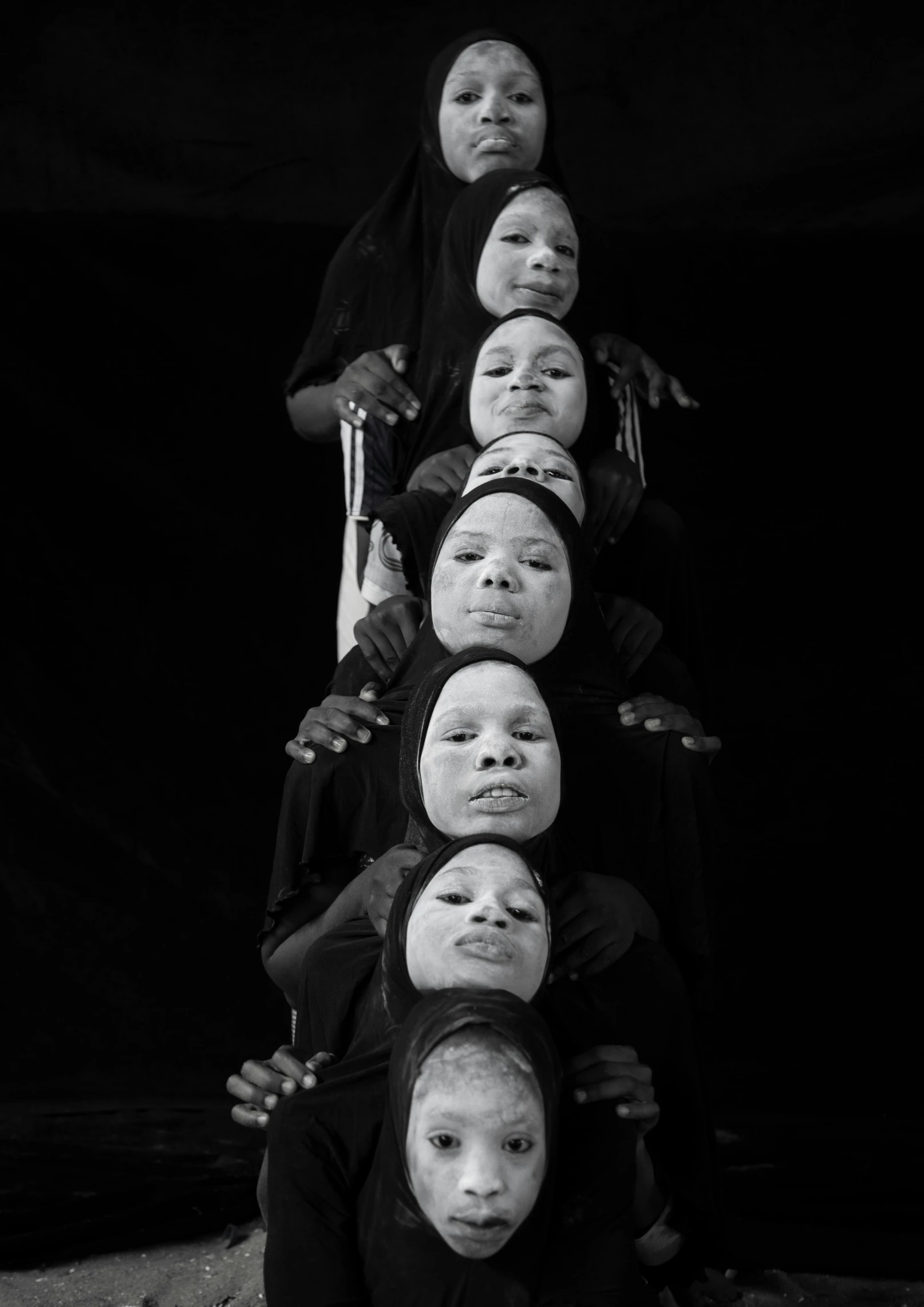 a group of people sitting on top of each other, an album cover, by Ibrahim Kodra, black scars on her face, vertical symmetry, black - and - white photograph, kano)