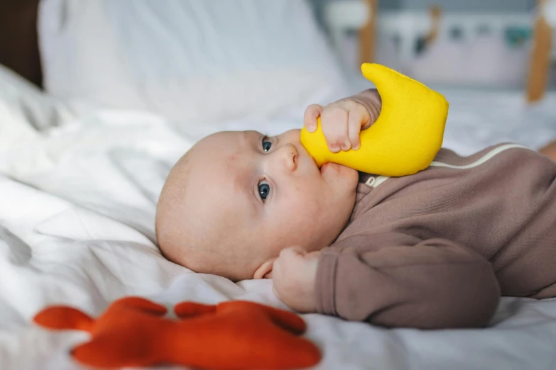 a baby laying on a bed with a rubber duck toy, inspired by Jacob Duck, dribble, multi - coloured, ergonomic, banana, silicone skin