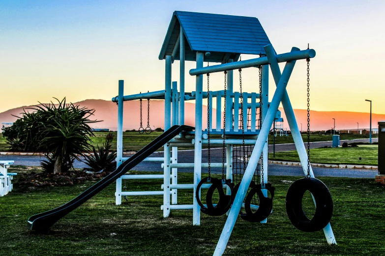a wooden swing set sitting on top of a lush green field, sunset beach, dingy gym, coloured photo, monument