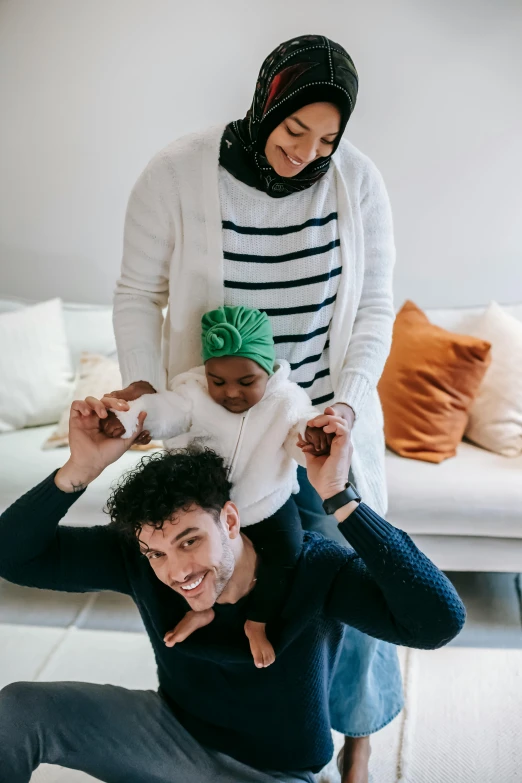 a man sitting on the floor next to a woman holding a baby, inspired by The Family Circus, pexels contest winner, renaissance, mixed race, pictured from the shoulders up, muslim, having fun