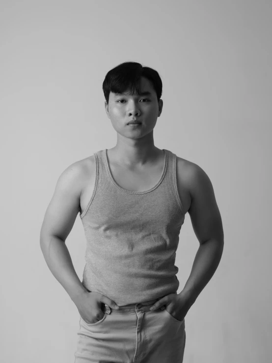 a man standing with his hands in his pockets, a black and white photo, inspired by Russell Dongjun Lu, wearing tank top, halfbody headshot, wearing a light shirt, lgbtq