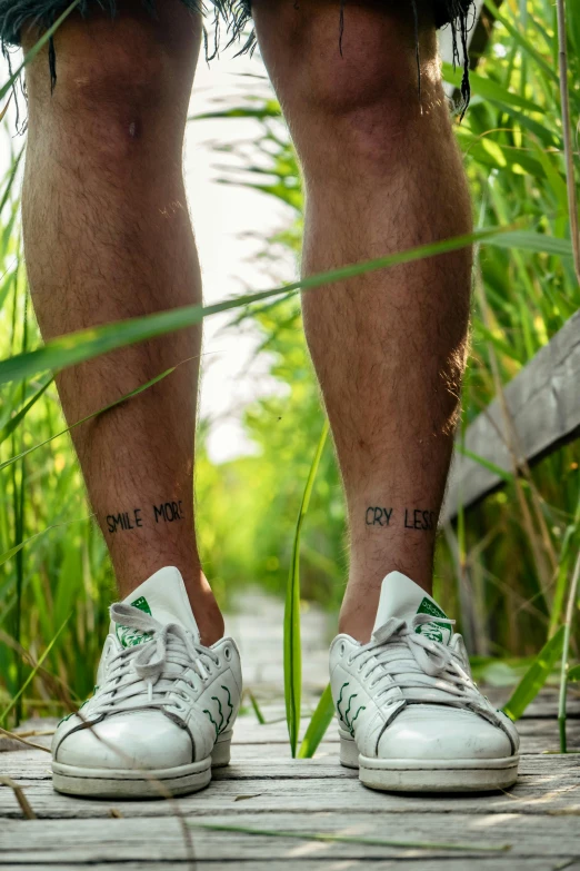 a man with tattoos on his legs standing on a boardwalk, a tattoo, by Jan Tengnagel, phragmites, green letters, midsommar - t, soccer player matthijs de ligt