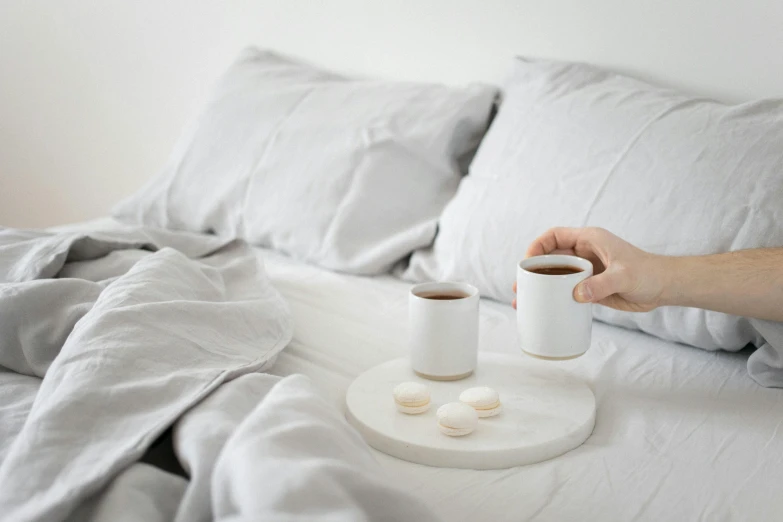 a person holding two cups of coffee on a tray on a bed, pexels contest winner, minimalism, organic ceramic white, moonlight grey, pills, textured base ; product photos