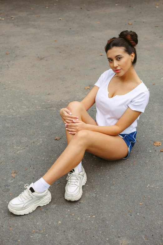 a woman sitting on the ground with her legs crossed, wearing white sneakers, posing for a picture, wearing tight shirt, wearing shorts