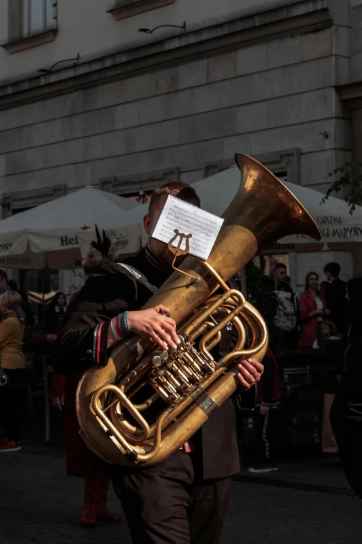 a man walking down a street holding a brass tuba, an album cover, by Carlo Martini, pexels contest winner, orange metal ears, 🚿🗝📝, in a city square, live performance