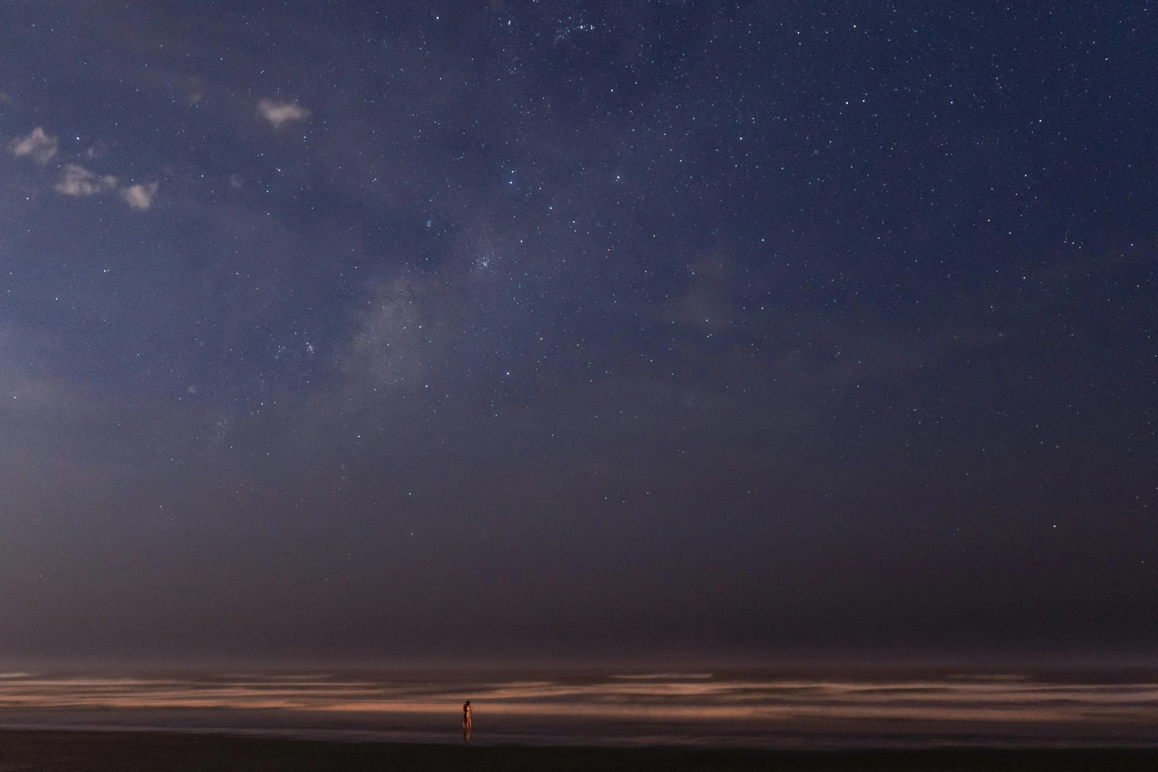 a man standing on top of a sandy beach under a night sky, vast expanse, oceanside, photograph