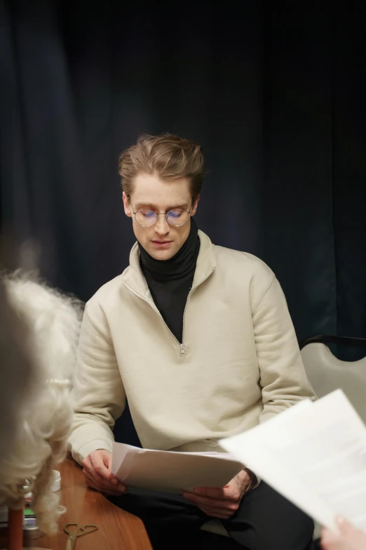 a group of people sitting around a wooden table, an album cover, by László Balogh, shutterstock, bauhaus, he is wearing a brown sweater, wearing white suit and glasses, delicate androgynous prince, attractive male playing piano