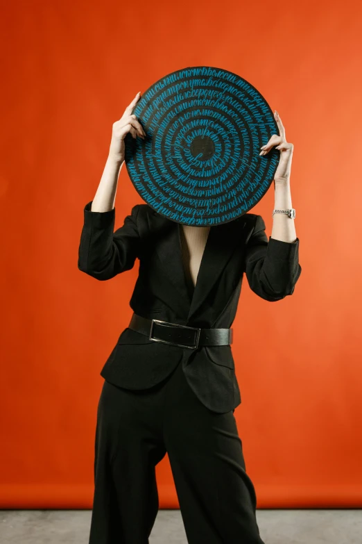 a woman in a black suit holding a blue plate over her head, pexels contest winner, conceptual art, orange and black, intricate outfit, non binary model, panel of black