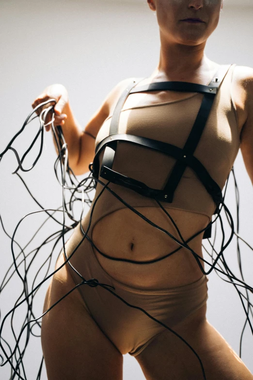 a woman that is holding some wires in her hands, an album cover, inspired by Hans Bellmer, unsplash, interactive art, skimpy leather armor, harnesses, singularity sculpted �ー etsy, performance