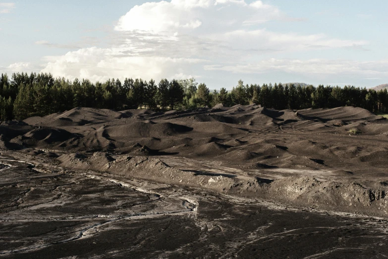 a dirt field with trees in the background, by Jesper Knudsen, unsplash contest winner, land art, flowing lava and ash piles, dunes, buildings covered in black tar, hedi slimane
